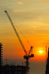 Silhouette of construction tower crane with sunset background at evening time.