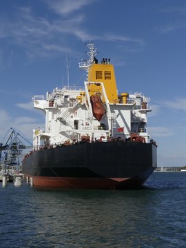 Products Tanker ship discharging at the Oil Terminal of Lorient, France, with black hull and yellow funnel on a sunny day. Vertical stern view