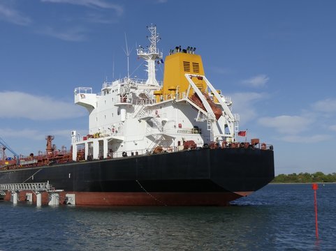 Products Tanker ship discharging at the Oil Terminal of Lorient, France, with black hull and yellow funnel on a sunny day. Horizontal stern view