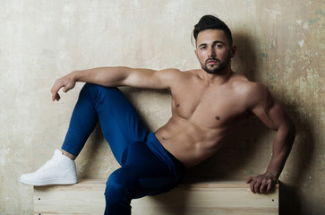 Handsome muscular man in blue sport pants on wooden stairs