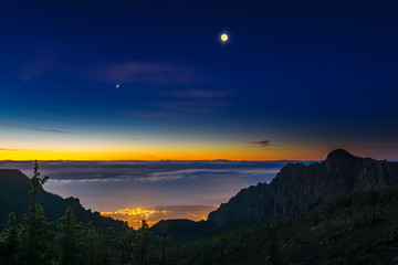 The hillside of the teide volcano lit by the setting sun, down the ocean and flowing sea of clouds