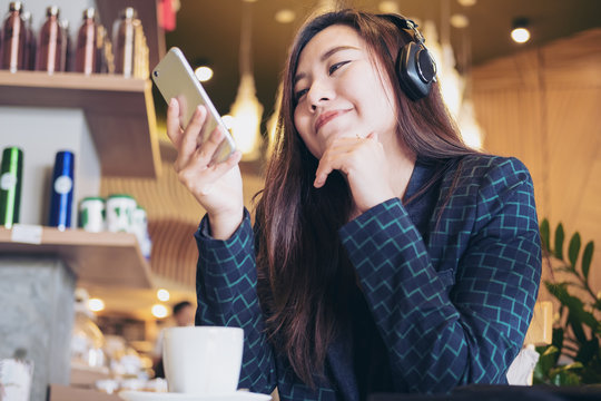 A beautiful Asian woman listening to music with headphone and holding smart phone with feeling happy and relax in modern cafe