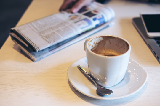 Closeup image of coffee cup , newspaper , laptop and smart phone on wooden table in coffee shop