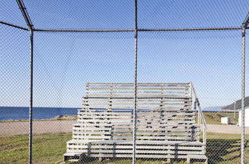 Rural Cape Breton, Nova Scotia, Canada baseball bleachers seen through backstop with the Gulf of St. Lawrence in the background.