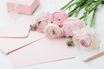 Envelope or letter, paper card, gift and pink ranunculus flowers on white table for greeting on...