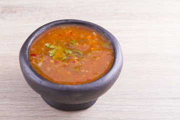 Spicy sauce in clay bowl on wood