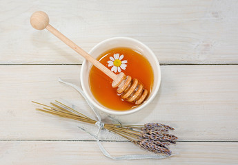 Bowl filled with flower honey and spoon with a cup of tea with chamomile flower