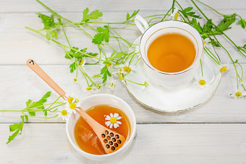 Bowl filled with flower honey and spoon with a cup of tea