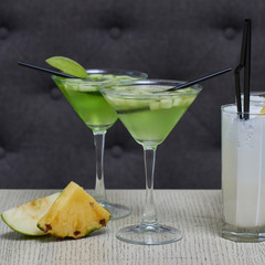 Apple martini and pina colada cocktails and apple and pineapple slices on table in cafe