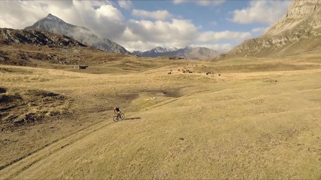 Aerial shot of mountain biker riding the trail on alpine pass in autumn season
