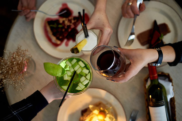 Girls party in cafe. Young woman drinking cocktails and wine and eating cakes. Female hands.