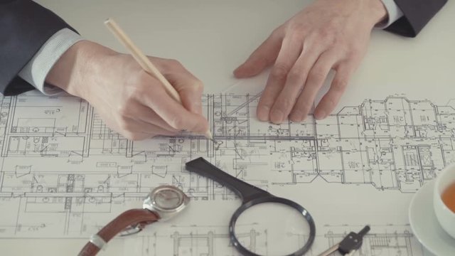 Architect sketching a construction project with pencil and ruler at work place.