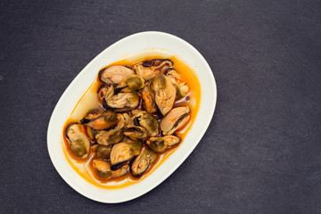 mussels in sauce on white dish on black wooden background