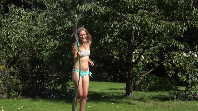 Playful sexy woman spraying herself with water on hot summer day holding hose above. 4K