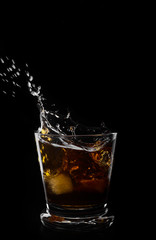 A glass of whiskey and ice cube on a black background