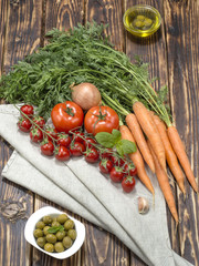 Olive oil with olives and vegetables on a wooden background. 