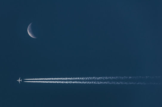 Crescent moon on the night sky near chemtrails from airplane; soft focus