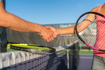 Tuinposter Tennis players shaking hands at court net at end of fun game. Man and woman playing recreational tennis handshaking with tennis racquets. © Maridav