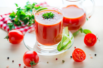 tomato juice in glass, jug with greenery, basil, cutted tomato fruit and dry pepper on light table, concept healthy eating, close up