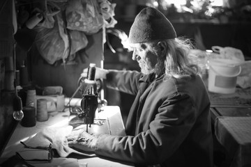 Old man sewing cloth bw
