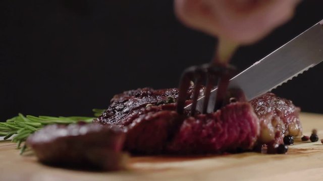 Slow motion. Juicy, fresh, appetizing beef steak cut with a knife, holding the fork. Close-up. Grilled sliced beef steak on cutting board.