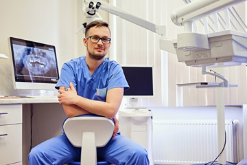 Male dentist in a room with medical equipment on background. - obrazy, fototapety, plakaty