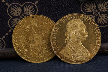 Close-up view of two on one another Austria-Hungary thalers, avers and revers of golden coin-ducats from 1915 with Kaiser Franz Joseph I, leaning on treasure chest and dark environment