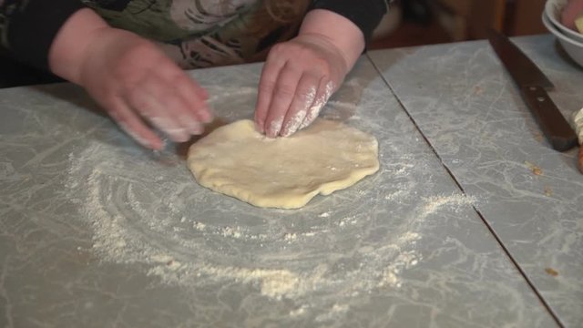 Female hands knead yeast dough for pizza or bread on a light kitchen table, close-up shot.
