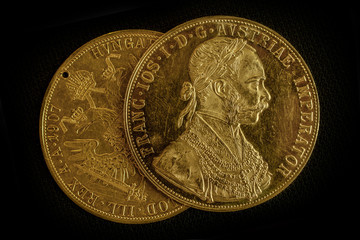 Close-up view of two on one another Austria-Hungary thalers, avers and revers of golden coin-ducats from 1915 with Kaiser Franz Joseph I, on dark background
