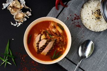 Korean cuisine. Spicy kimchi soup served in a bowl standing on black background.