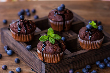 Chocolate muffins with chocolate syrup, blueberries and mint in a wooden background