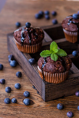 Chocolate muffins with chocolate syrup, blueberries and mint in a wooden background