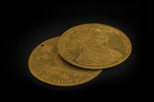 Close-up view in perspective of two on one another Austria-Hungary thalers, avers and revers of golden coin-ducats from 1915 with Kaiser Franz Joseph I, on dark background
