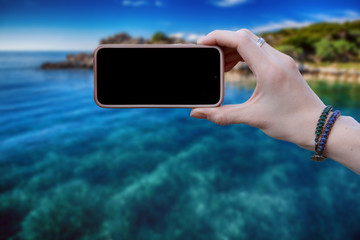 Woman using smartphone to take a picture of green tropical island. Vintage style. The screen is black