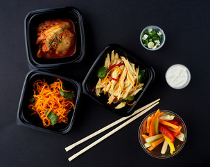 Korean cuisine. Set of salads on black background. Asparagus, korean carrot, kaktugi, fresh vegetable sticks and green onion.