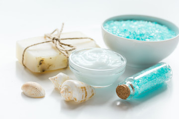 blue bath salt, body cream and shells for spa on white table background