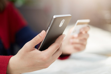A close-up of female`s hands holding smartphone and credit card paying bill online via internet, making transaction, using mobile bank application on cell phone. Modern technology and online payment.