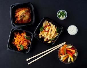 Korean cuisine. Set of salads on black background. Asparagus, korean carrot, kaktugi, fresh vegetable sticks and green onion.
