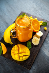 Fresh Orange smoothie drink with banana, mango, carrots on black wooden board.
