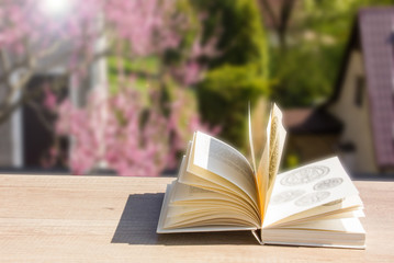 Open book on wooden table over spring garden