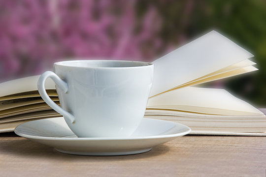 Coffee cup with open book over spring garden