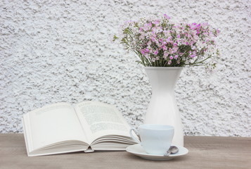 Book, white cup and vase with flowers on wooden table