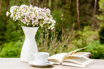 Book, white cup and vase with flowers on wooden table