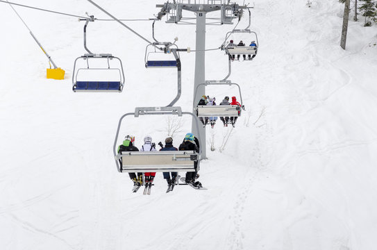 People ride the ski chair lift up the mountain together while sitting closely to each other having a fun time during a day of snowboarding