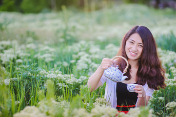 Young Chinese girl pouring tea in flowering meadow