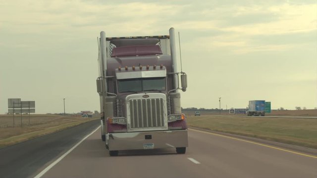 FPV CLOSE UP: Being overtaken by container semi truck driving along the multiple lane highway in US countryside. Freight semi-truck transporting goods, people on road trip traveling in sunny summer
