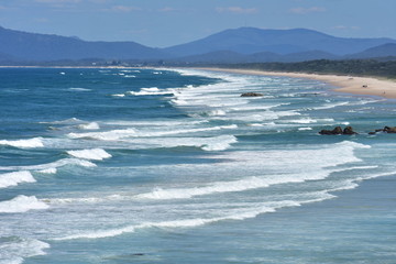 Sandy beach with white oceanic surf south from Tacking Point Lighthouse in Port Macquarie with Three Brothers in far background.
