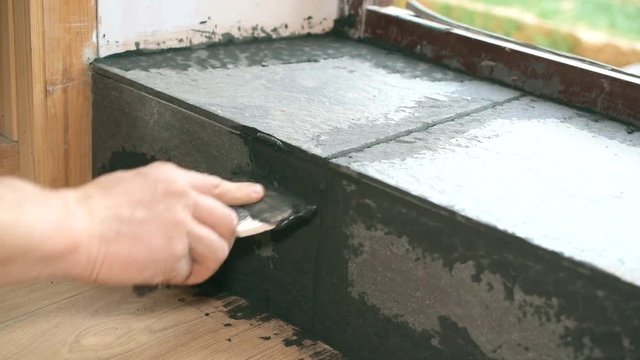 Hands of tile worker filling gaps between tiles with a grout using soft rubber spattle in threshold