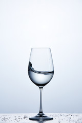 Pure water wave in the wine glass while standing on the glass with drapes against light background.