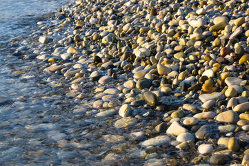 sea pebble beach with multicoloured stones, waves with foam